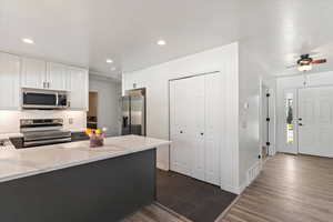 Kitchen with white cabinetry, stainless steel appliances, light stone counters, dark wood-type flooring, and a peninsula