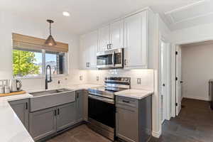 Kitchen featuring two tone cabinets, stainless steel appliances, light stone counters, decorative backsplash, and hanging light fixtures