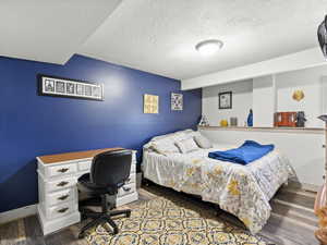 Bedroom with a textured ceiling, dark wood-style flooring, and a desk