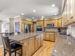 Kitchen featuring light wood-style floors, dark stone counters, stainless steel appliances, backsplash, and a center island