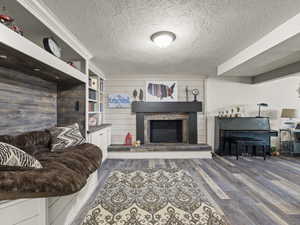 Living room with dark wood-type flooring, a textured ceiling, and a fireplace with raised hearth