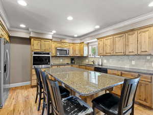 Kitchen featuring a kitchen breakfast bar, dark stone countertops, a kitchen island, black appliances, and light wood-type flooring