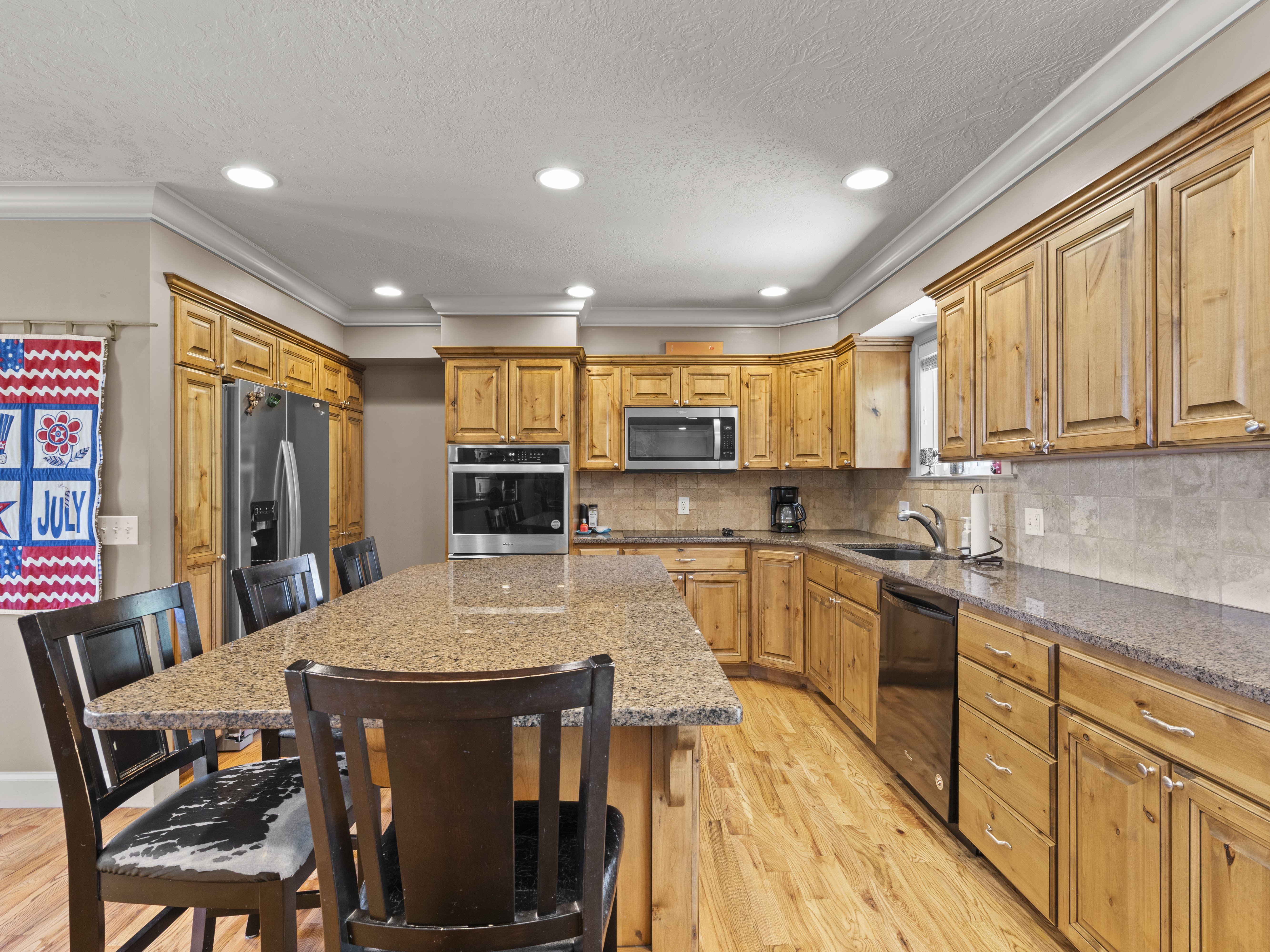 Kitchen with a kitchen island, light wood-type flooring, a breakfast bar, black appliances, and dark stone countertops