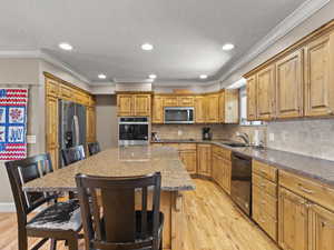Kitchen with a kitchen island, light wood-type flooring, a breakfast bar, black appliances, and dark stone countertops