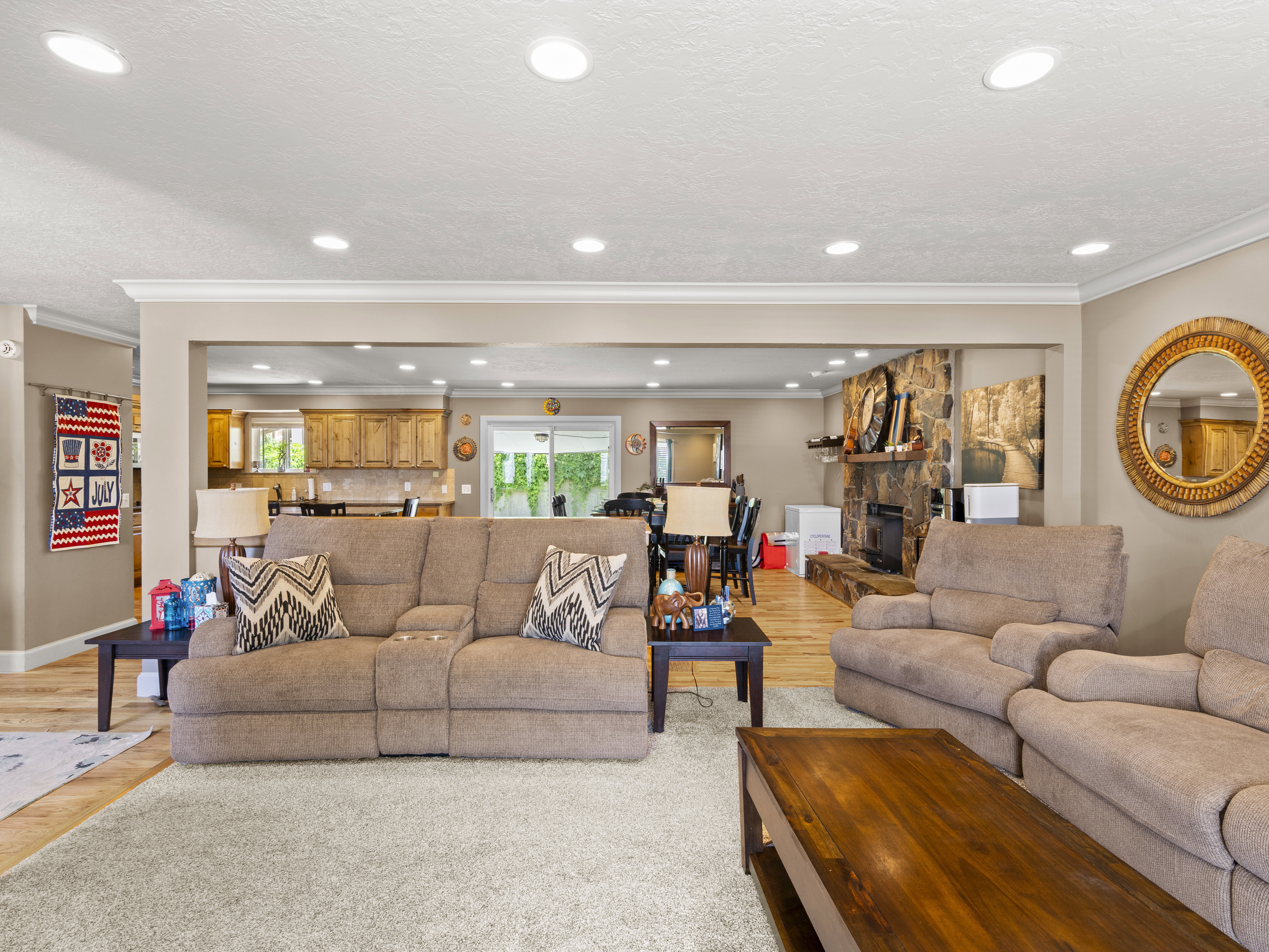 Living room featuring light wood-style floors, a stone fireplace, ornamental molding, and recessed lighting