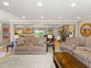 Living room featuring light wood-style floors, a stone fireplace, ornamental molding, and recessed lighting