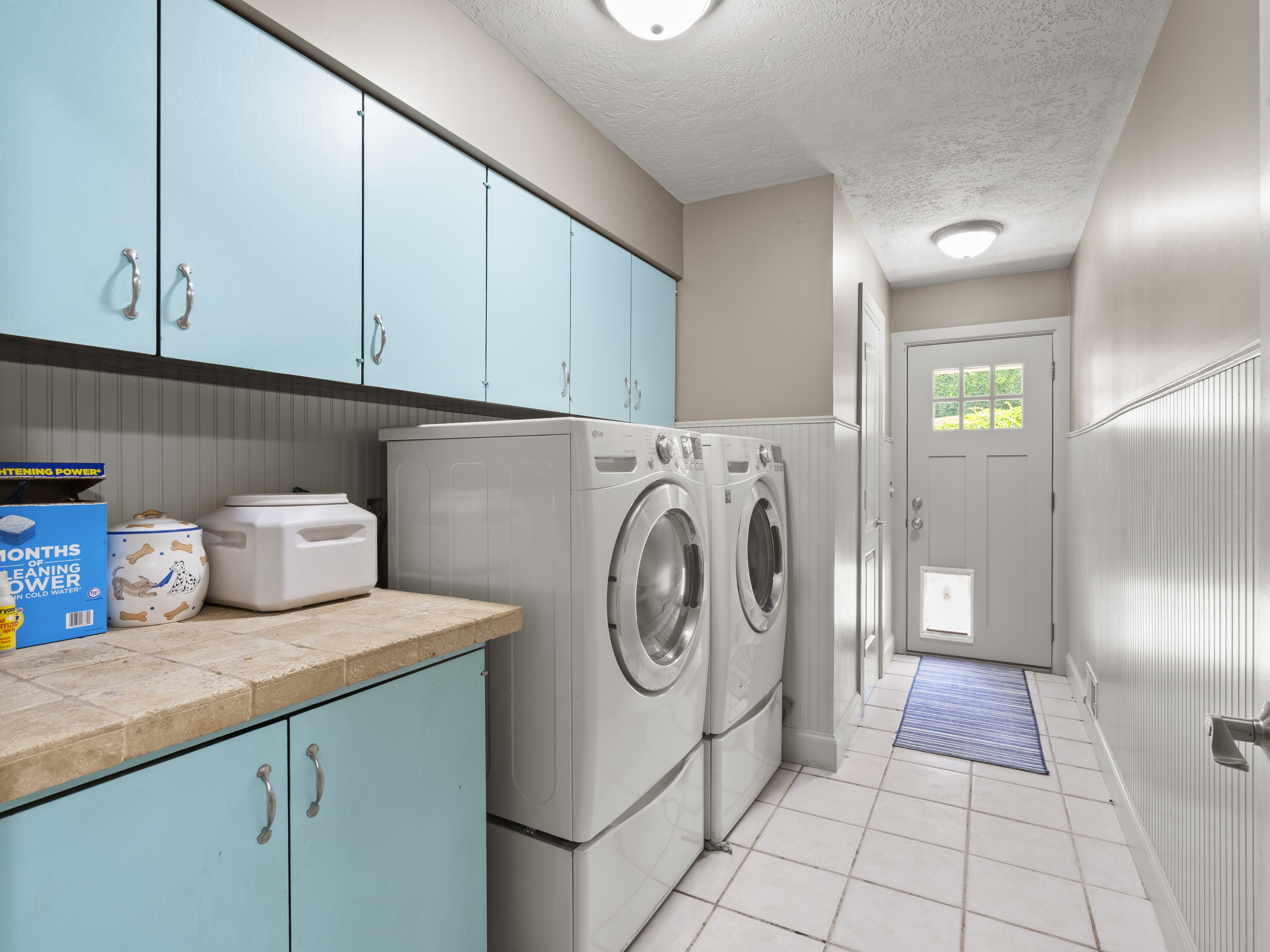 Laundry area featuring a wainscoted wall, cabinet space, a textured ceiling, light tile patterned floors, and washing machine and clothes dryer