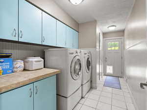 Laundry area featuring a wainscoted wall, cabinet space, a textured ceiling, light tile patterned floors, and washing machine and clothes dryer