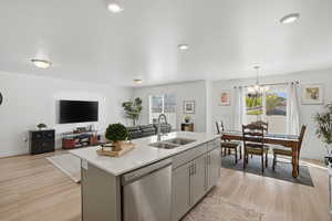Kitchen with open floor plan, stainless steel dishwasher, a kitchen island with sink, gray cabinetry, and light stone countertops