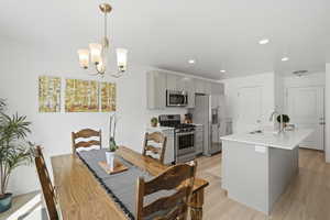 Kitchen with gray cabinets, stainless steel appliances, a center island with sink, and light flooring
