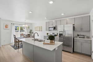 Kitchen featuring gray cabinets, stainless steel appliances, light stone counters, recessed lighting, and an island with sink