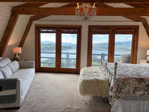 Carpeted bedroom featuring access to outside, a water and mountain view, wooden walls, suspended lighting, and a wood ceiling with exposed beams