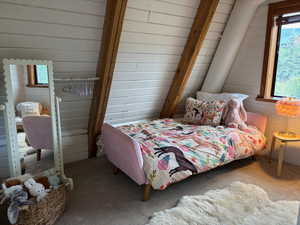 Carpeted bedroom featuring wooden walls, multiple windows, and lofted ceiling