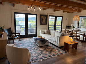 Living room with french doors, beam ceiling, wooden walls, healthy amount of natural light, and wood finished floors