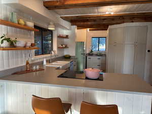 Kitchen with a peninsula, freestanding refrigerator, open shelves, a wooden ceiling with exposed beams, and a breakfast bar