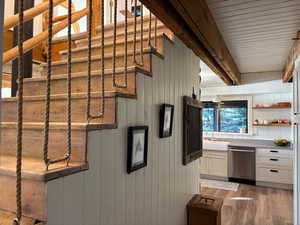 Kitchen featuring light wood-style floors, dishwasher, open shelves, white cabinetry, and wood walls