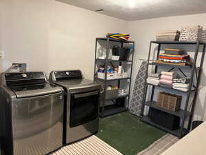 Laundry area with a textured ceiling, washing machine and clothes dryer, and concrete floors