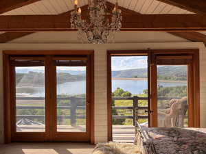 Doorway to outside with a water and mountain view, suspended lighting, carpet flooring, wooden walls, and a wooden ceiling with exposed beams