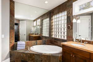 Full bath featuring two vanities, a garden tub, plenty of natural light, and recessed lighting