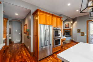 Kitchen featuring arched walkways, stainless steel appliances, recessed lighting, dark wood-style flooring, and wood finish cabinetry