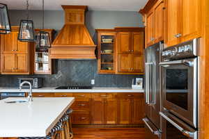 Kitchen with wood finish cabinets, stainless steel appliances, pendant lighting, a textured ceiling, and glass fronted cabinets