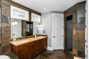 Full bathroom with double vanity, a stall shower, dark stone finish floors, and a textured ceiling