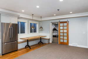 Kitchen with high quality fridge, crown molding, a barn door, light wood-type flooring, and hanging light fixtures