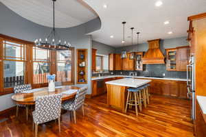 Kitchen featuring glass fronted cabinets, a kitchen island with sink, wood finish cabinets, suspended lighting, and dark wood-style flooring