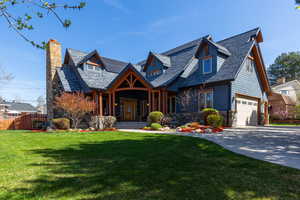 View of front facade featuring a porch, a chimney, stone siding, a garage, and concrete driveway
