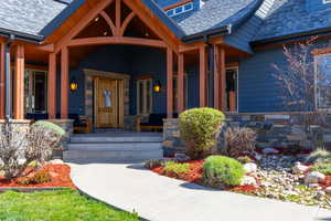 Doorway to property with covered porch, stone siding, and a shingled roof
