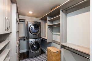 Laundry area with stacked washer / dryer, dark wood finished floors, a textured ceiling, and crown molding