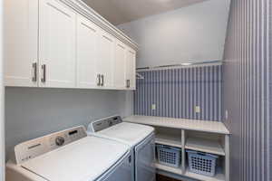 Laundry area featuring washing machine and dryer, cabinet space, and a textured wall