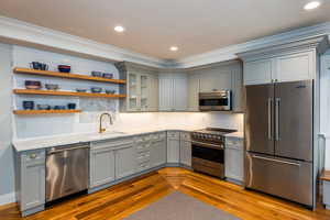 Kitchen featuring premium appliances, light stone counters, gray cabinets, dark wood-style floors, and ornamental molding