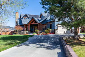 View of front of house featuring a garage, stone siding, a porch, a chimney, and driveway