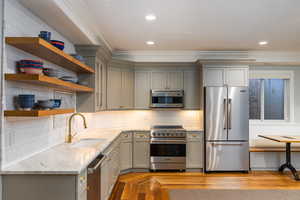Kitchen with light stone counters, high end appliances, light wood-type flooring, gray cabinets, and ornamental molding