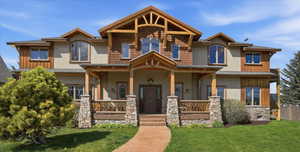 Craftsman inspired home featuring covered porch, stucco siding, a front yard, and stone siding