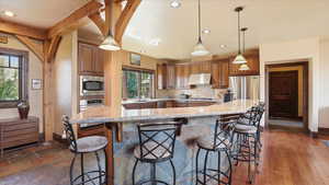 Kitchen with a breakfast bar area, hanging light fixtures, wood finish cabinetry, stainless steel appliances, and light stone countertops