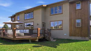 Back of house featuring a lawn, a wooden deck, and stucco siding