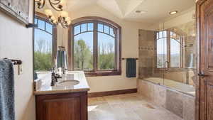 Bathroom with stone tile floors, double vanity, tiled shower / bath, and suspended lighting