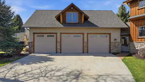 View of front of home featuring a shingled roof, stone siding, concrete driveway, and a garage