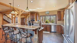 Kitchen featuring wood finish cabinetry, a breakfast bar, stainless steel appliances, hanging light fixtures, and light stone counters