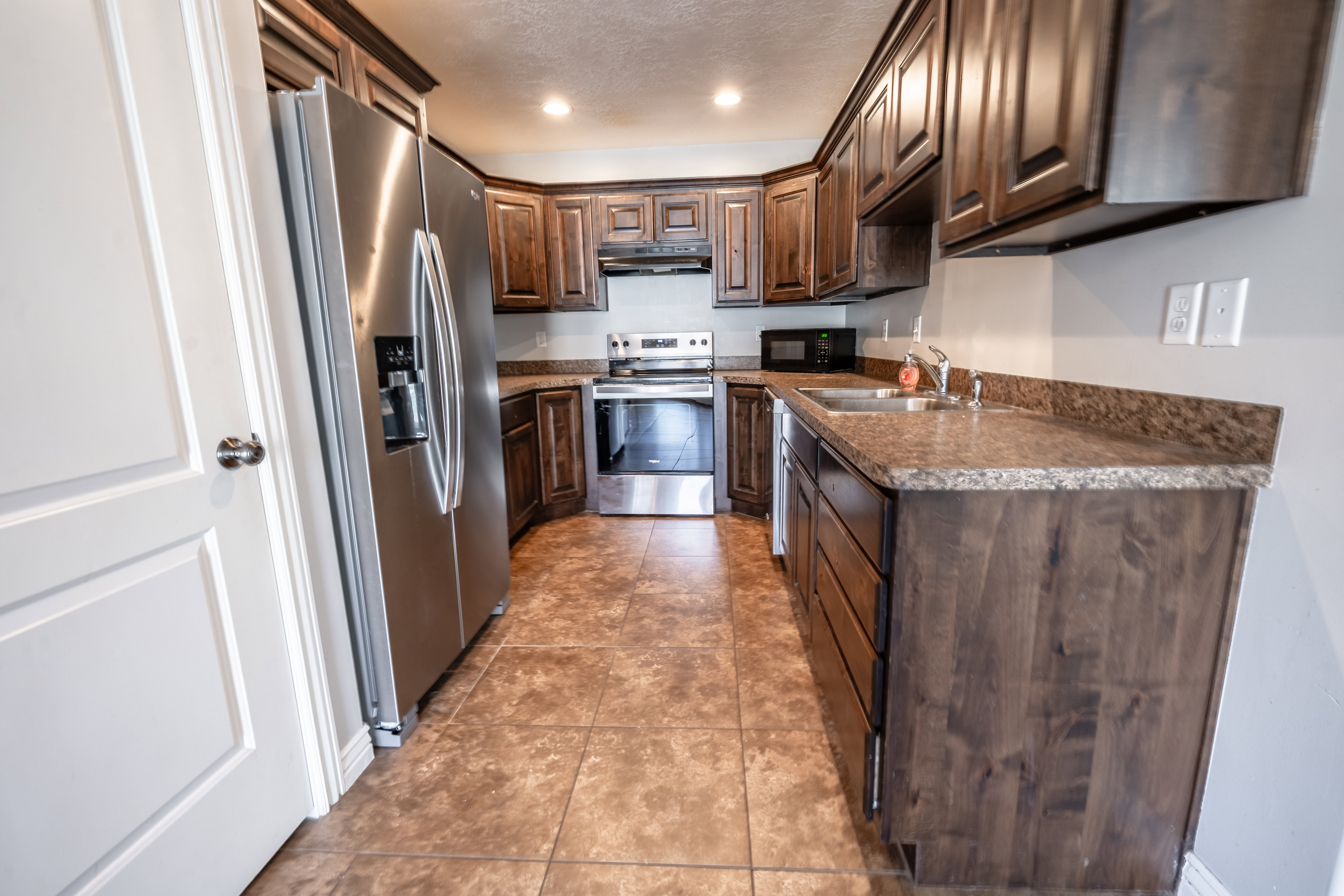 Kitchen with stainless steel appliances, dark wood finish cabinetry, recessed lighting, light tile patterned floors, and a textured ceiling