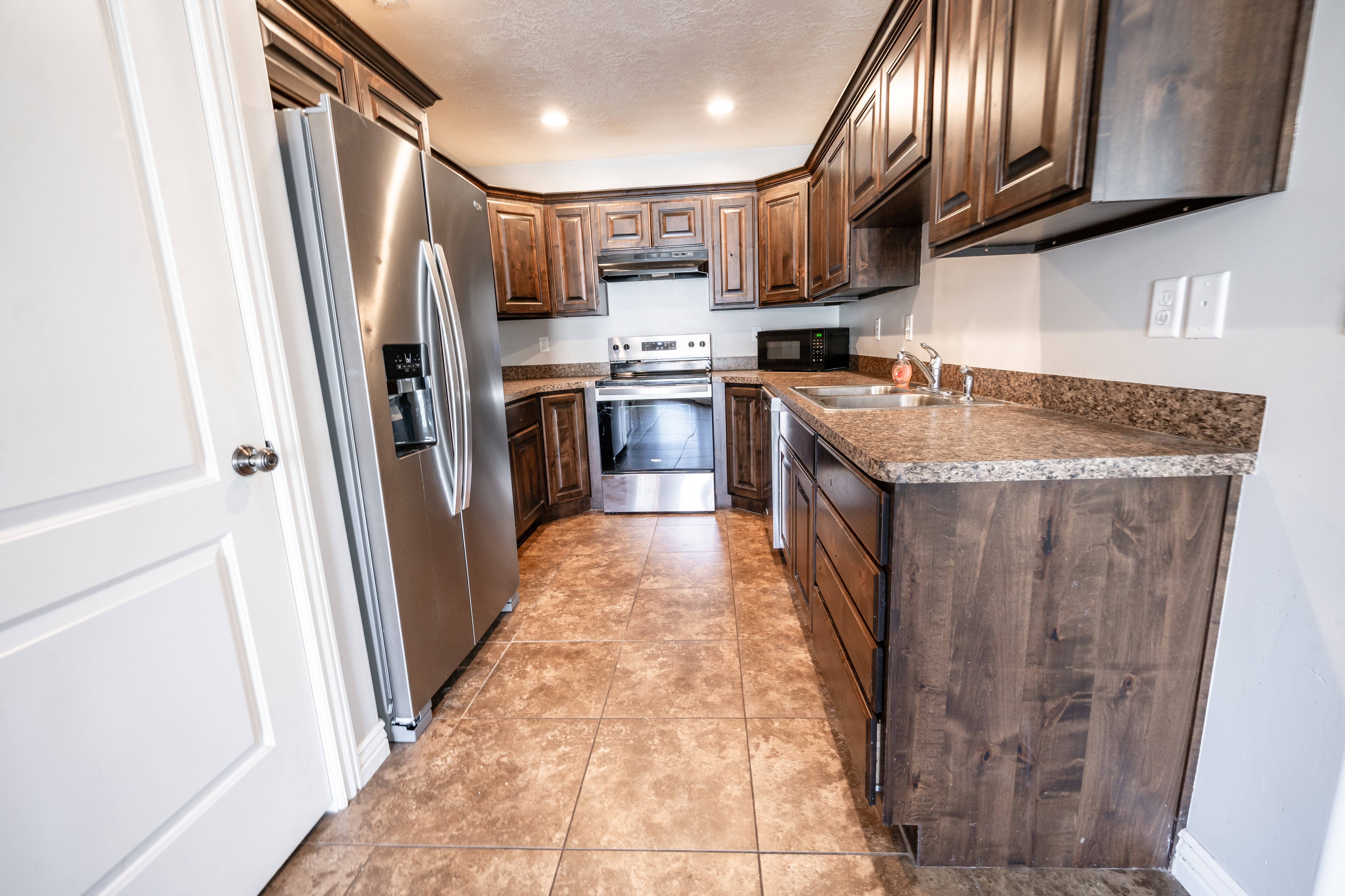 Kitchen featuring stainless steel appliances, dark wood finish cabinets, recessed lighting, light tile patterned flooring, and dark countertops