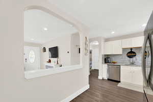 Kitchen with stainless steel appliances, arched walkways, white cabinets, decorative backsplash, and dark wood-type flooring