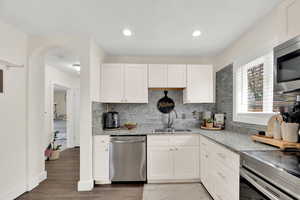 Kitchen featuring stainless steel appliances, white cabinets, light stone counters, recessed lighting, and decorative backsplash