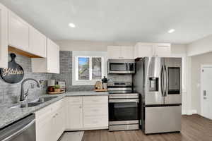 Kitchen with light stone counters, stainless steel appliances, white cabinets, light wood finished floors, and recessed lighting