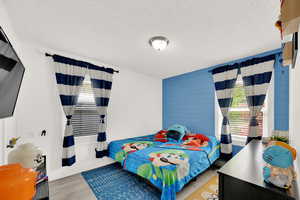 Bedroom with light wood-style flooring, a textured ceiling, and multiple windows