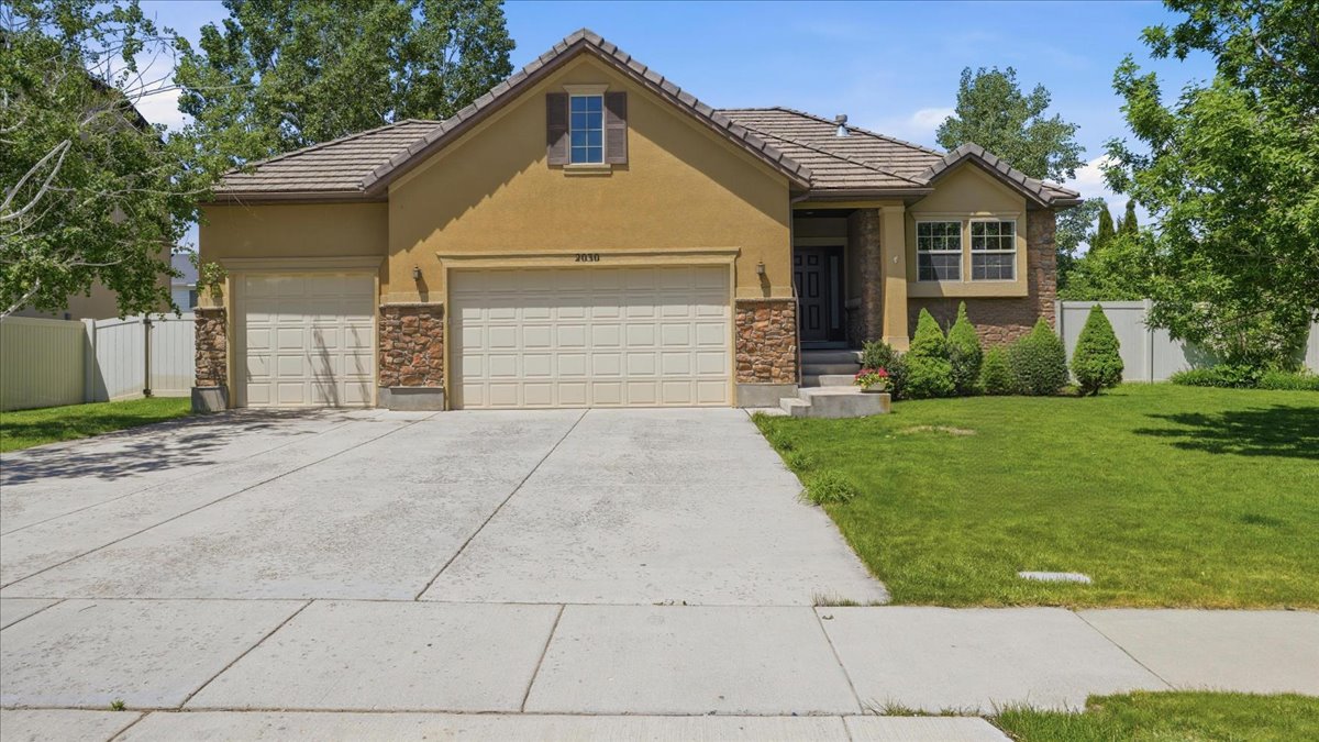 Stucco and stone facade home featuring a three-car garage and a concrete driveway