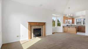Unfurnished living room featuring light colored carpet, lofted ceiling, hanging lights, and a tiled fireplace
