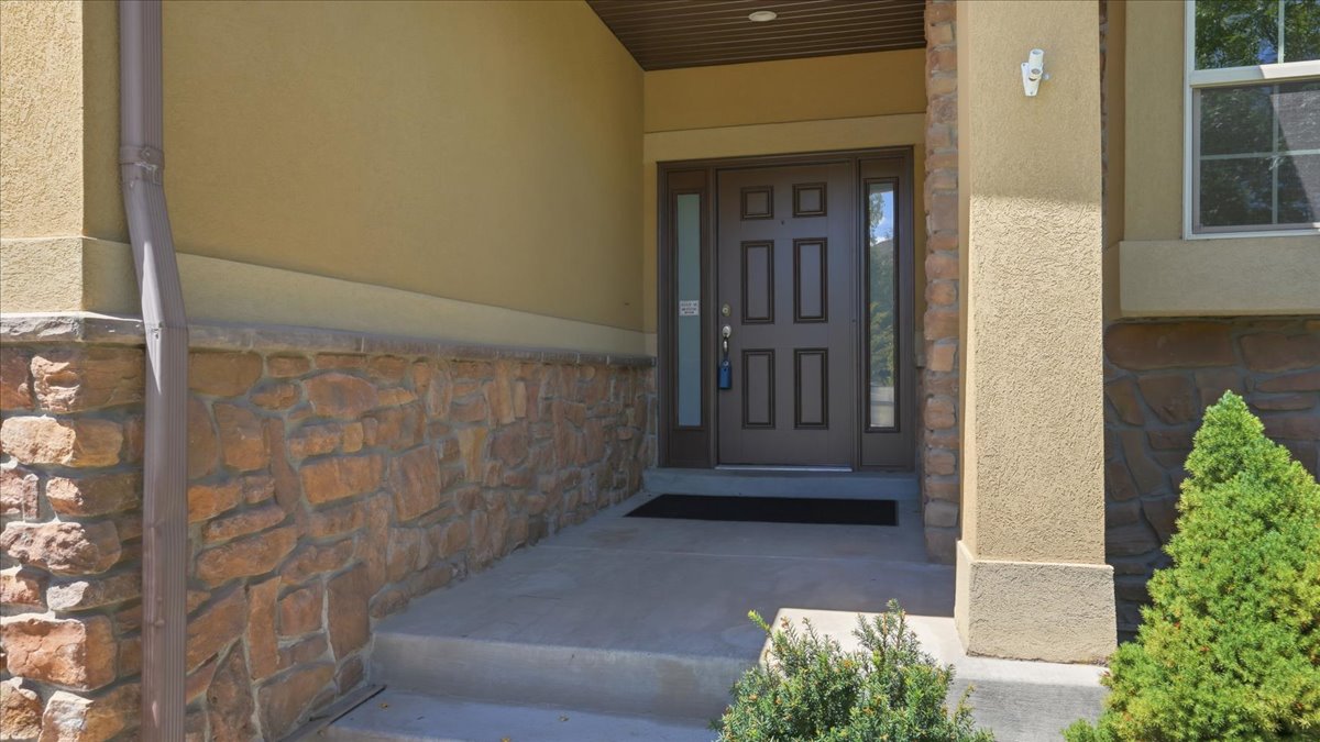 Entryway featuring a panel door with sidelights, a textured stucco exterior, and a stone veneer foundation
